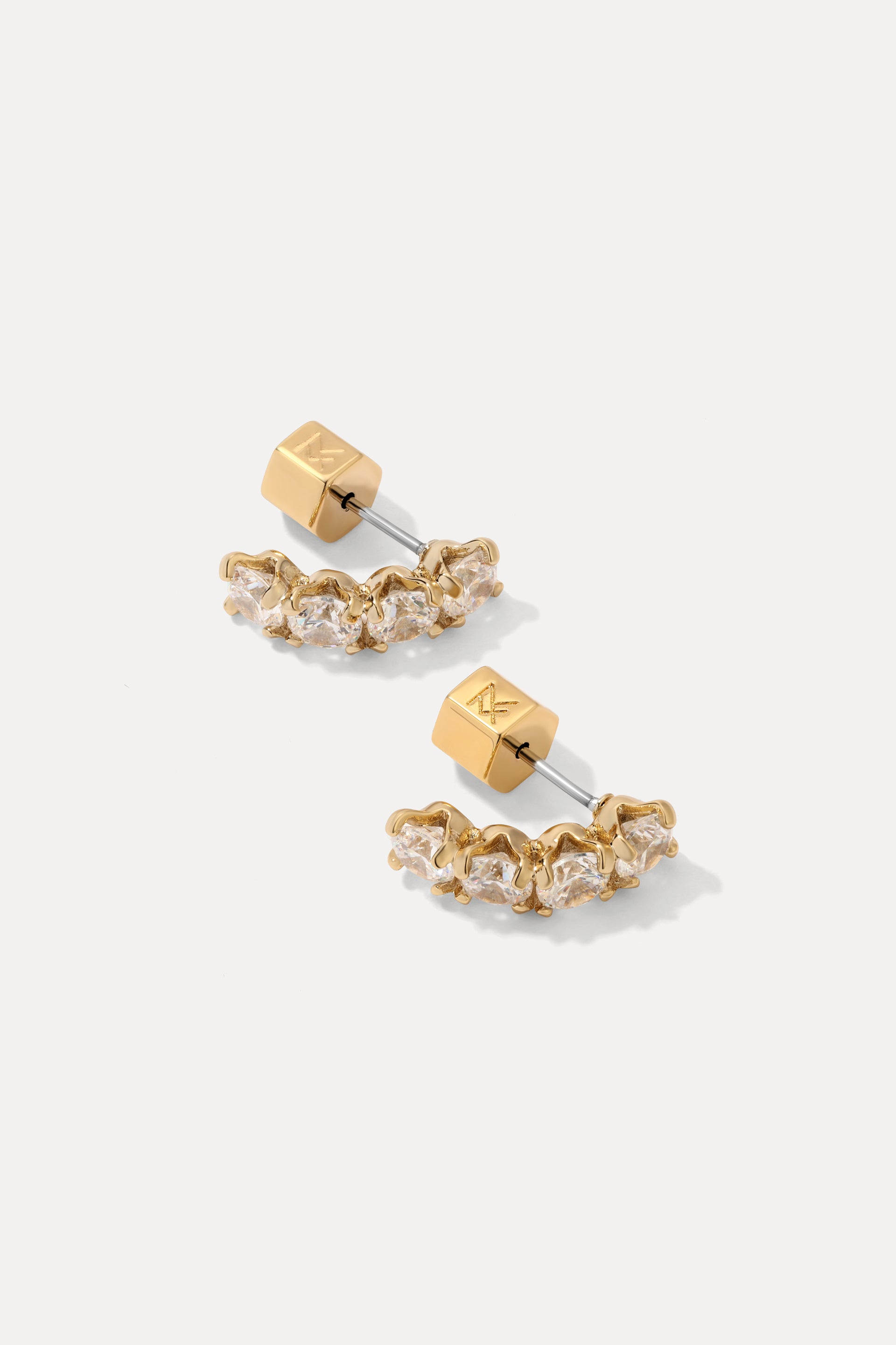 Pair of gold Ansley curved stud earrings set with round cubic zirconias on a plain background.