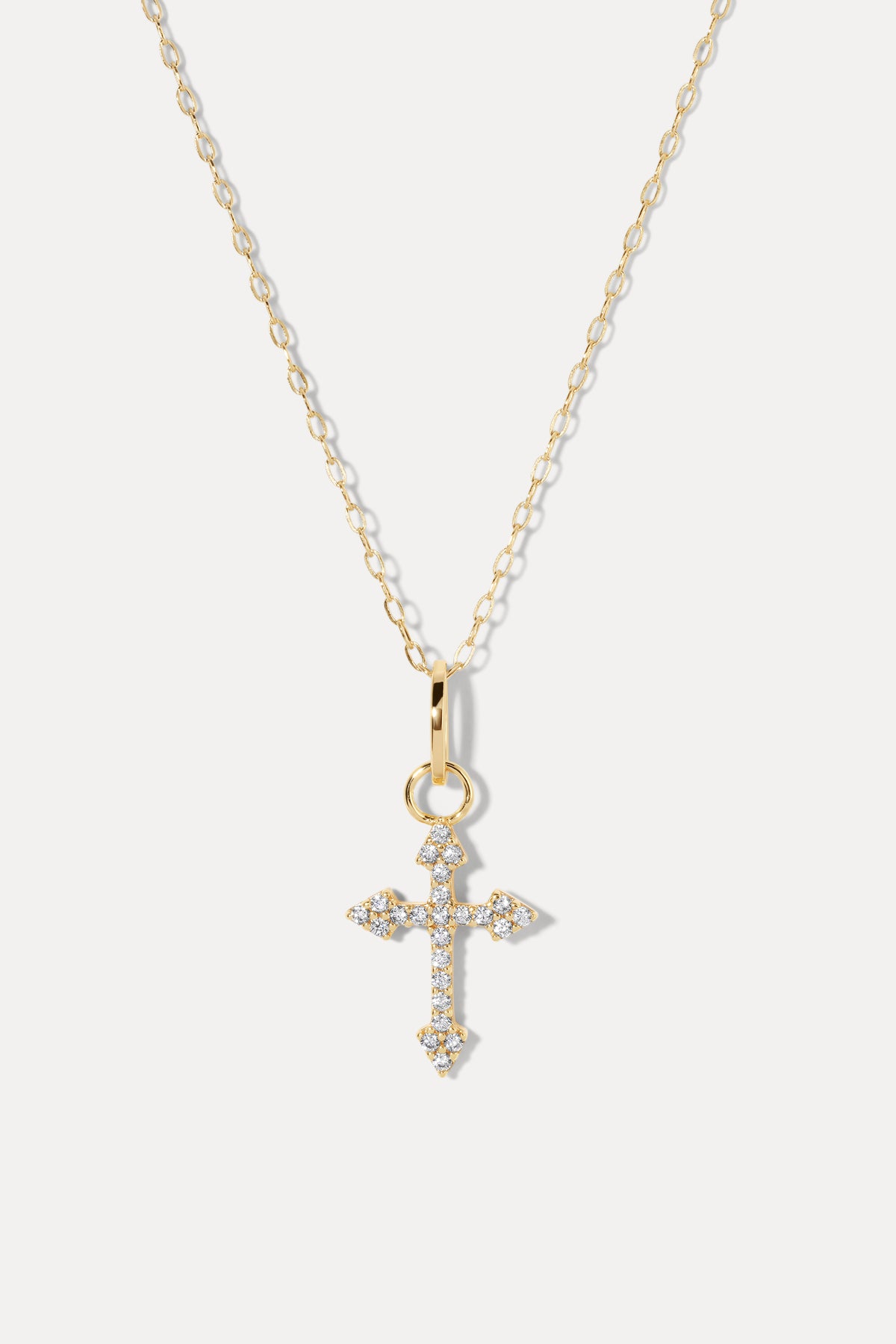 Gold cross pendant with sparkling stones and arrow ends attached to a thin chain on white background.