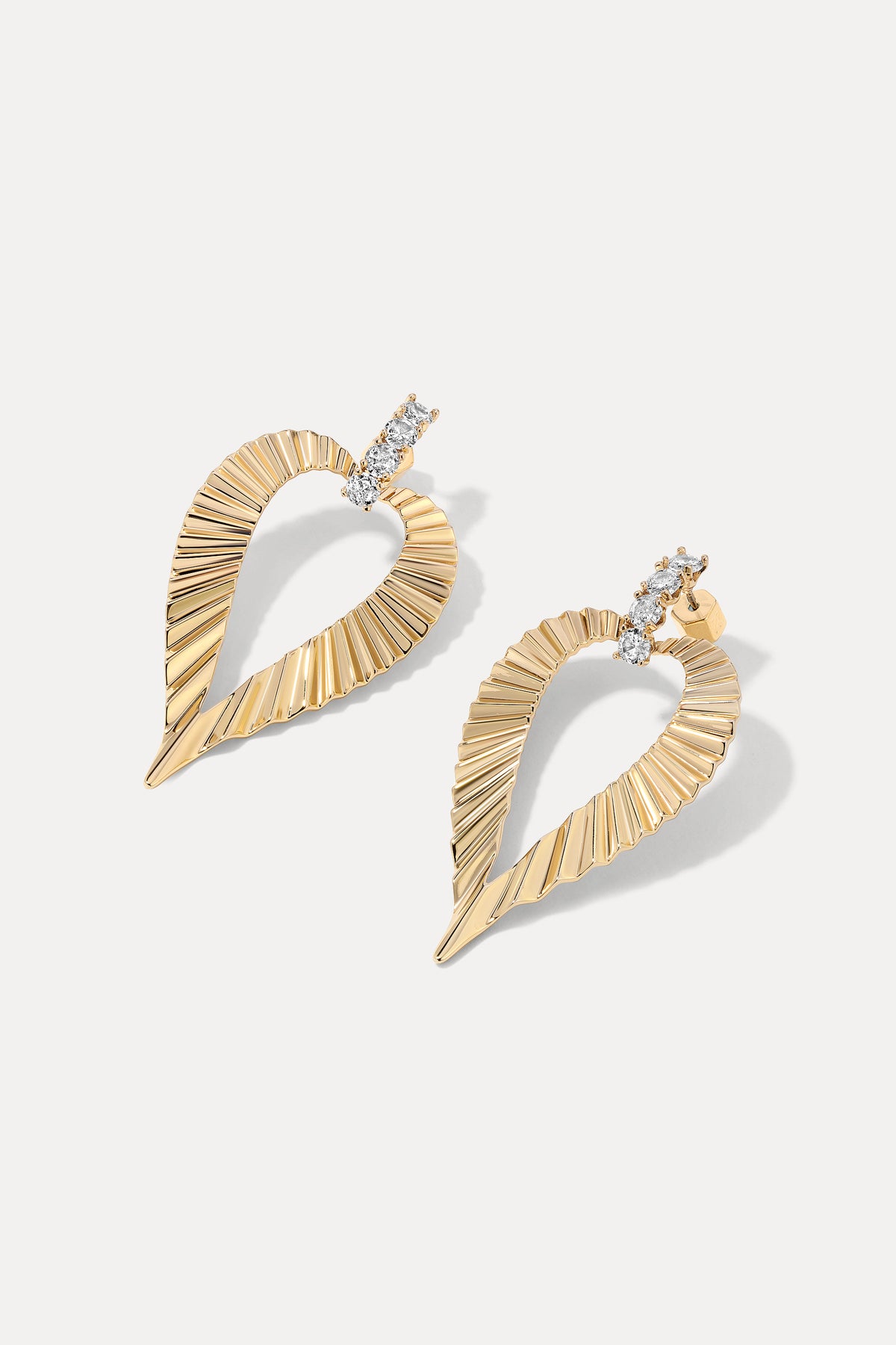 Pair of gold Jasmine Earrings with crystal studs and ribbed heart drop on white.