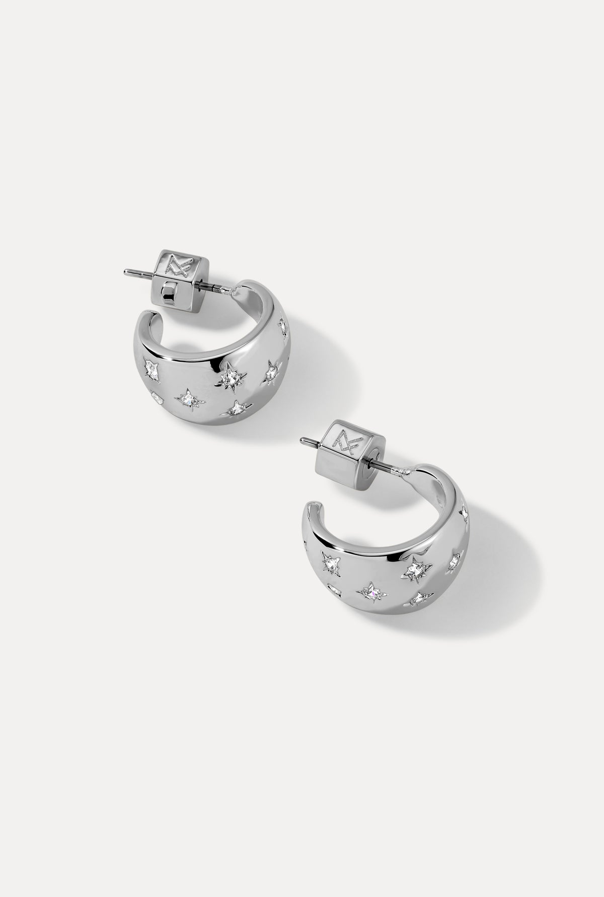 Pair of silver Lunette Huggies with starburst cubic zirconia settings on white background.