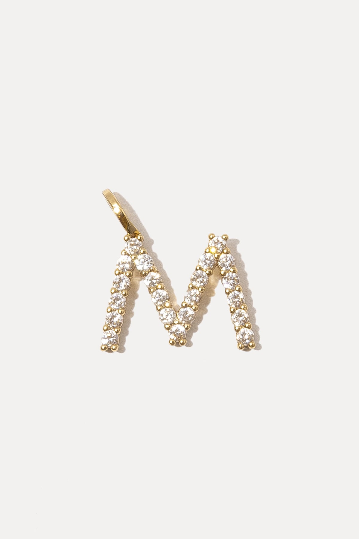 Gold pave initial charm in the letter M with crystal stones on a bail against a plain white background.