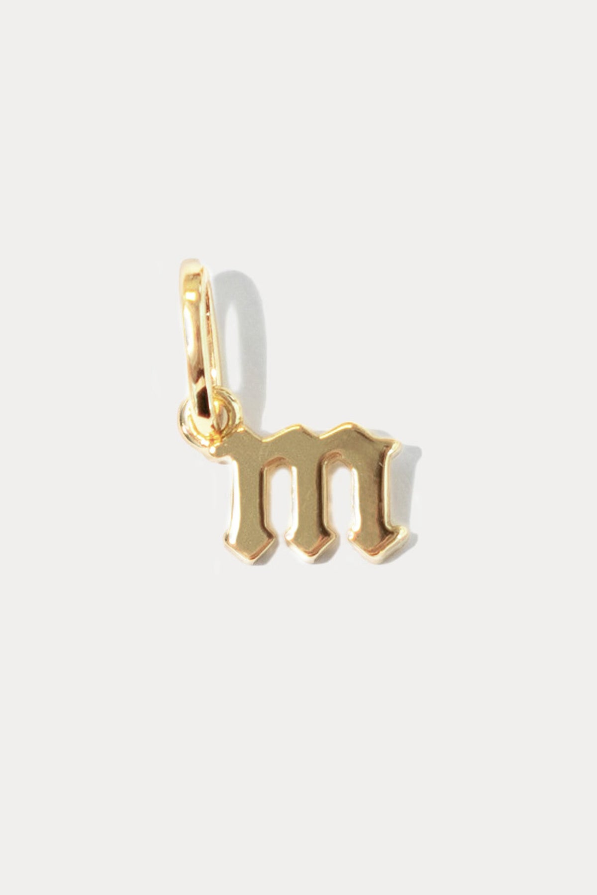Petite gold gothic initial charm in the letter "m" on a bail against a plain white background.