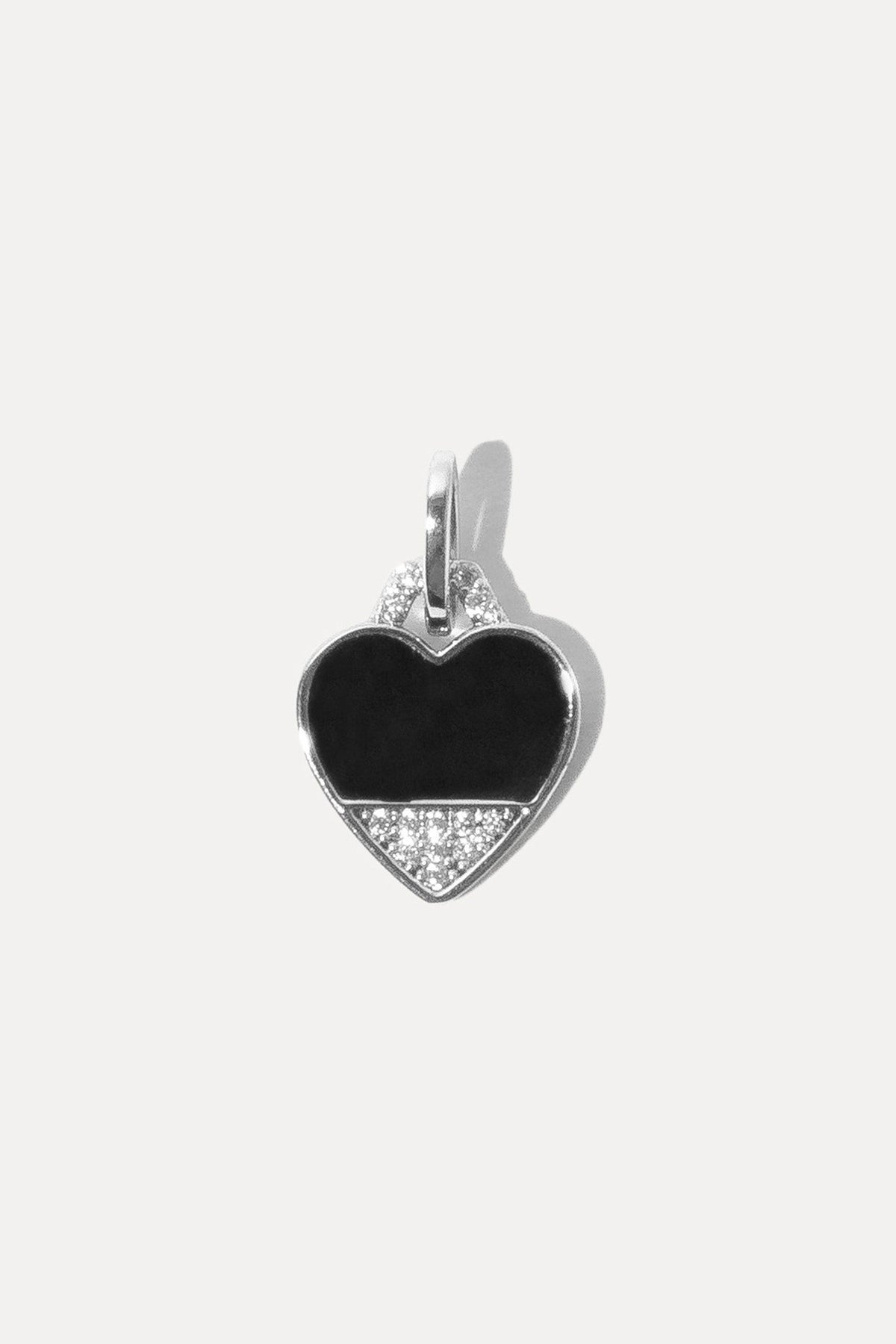 Silver heart charm filled with black enamel and a central clear stone on a bail against plain white background.