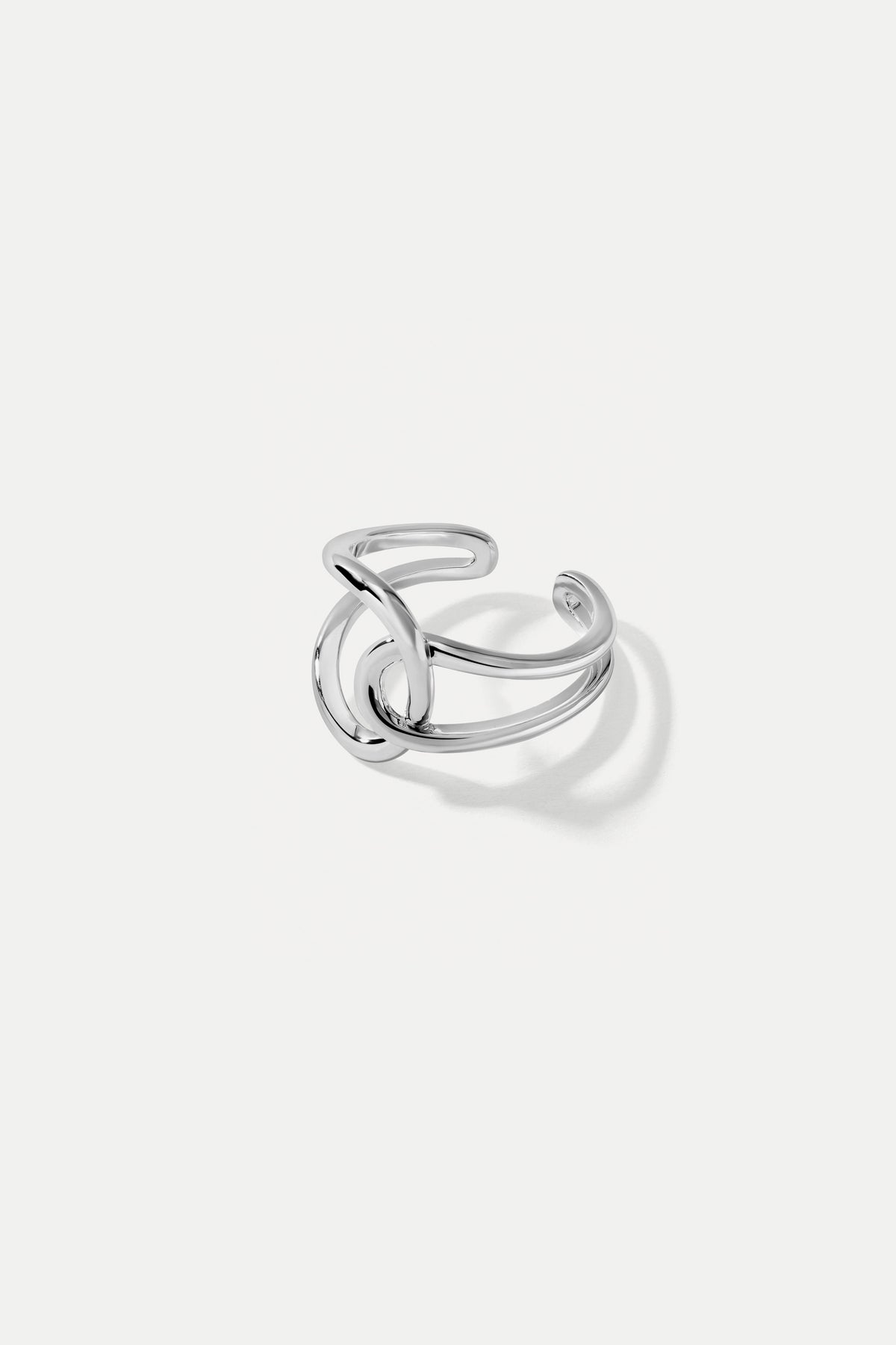 Silver Celine open band ring with a sculptural intertwined loop design featured on a white backdrop.