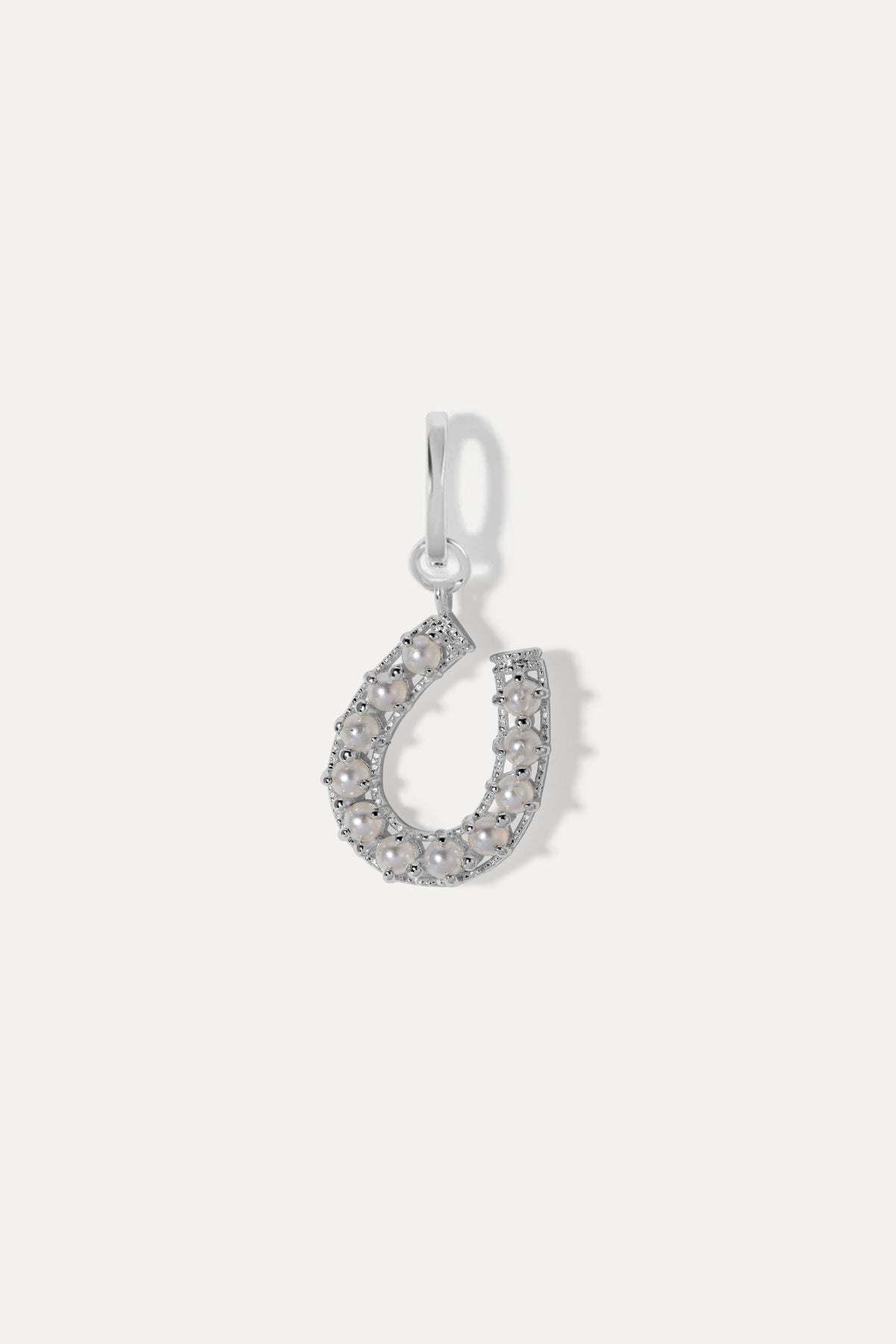 Silver horseshoe charm inset with small pearls on a bail against a plain white background.