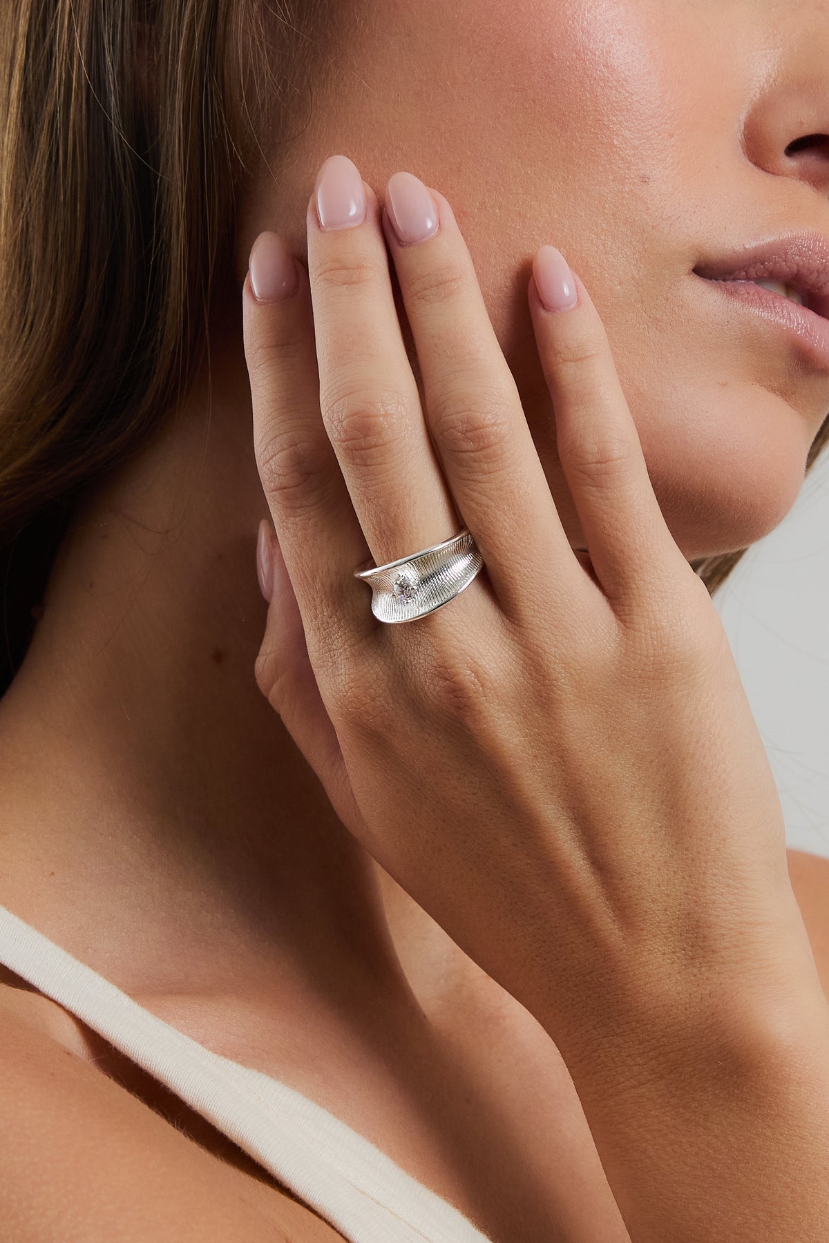 Model wearing silver Anne Marie ring set with a CZ stone, resting hand against face in a cream tank top.