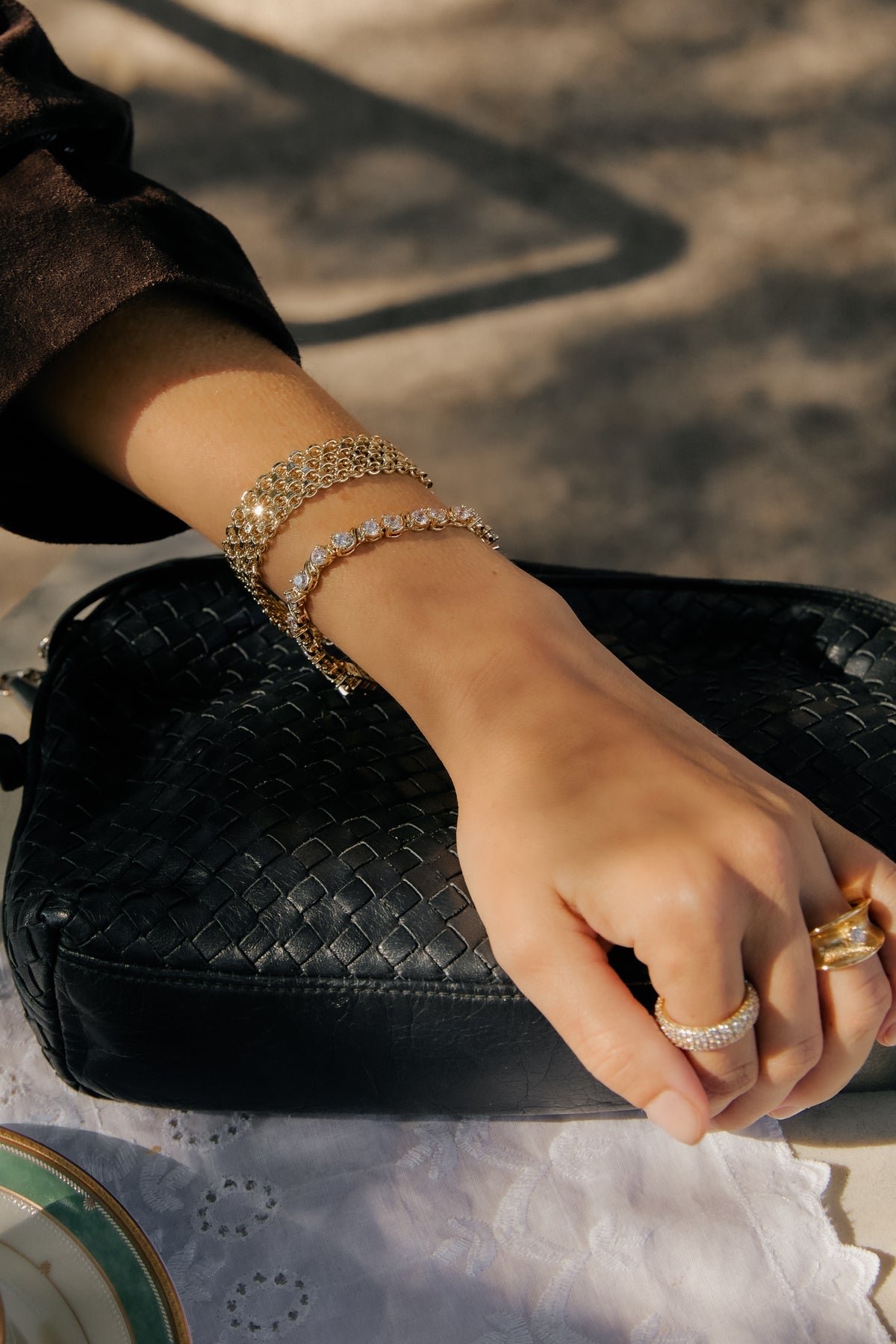 Model wearing gold Camryn woven bracelet, Delilah tennis bracelet, Vivienne ring, and Ann Marie ring on a black bag