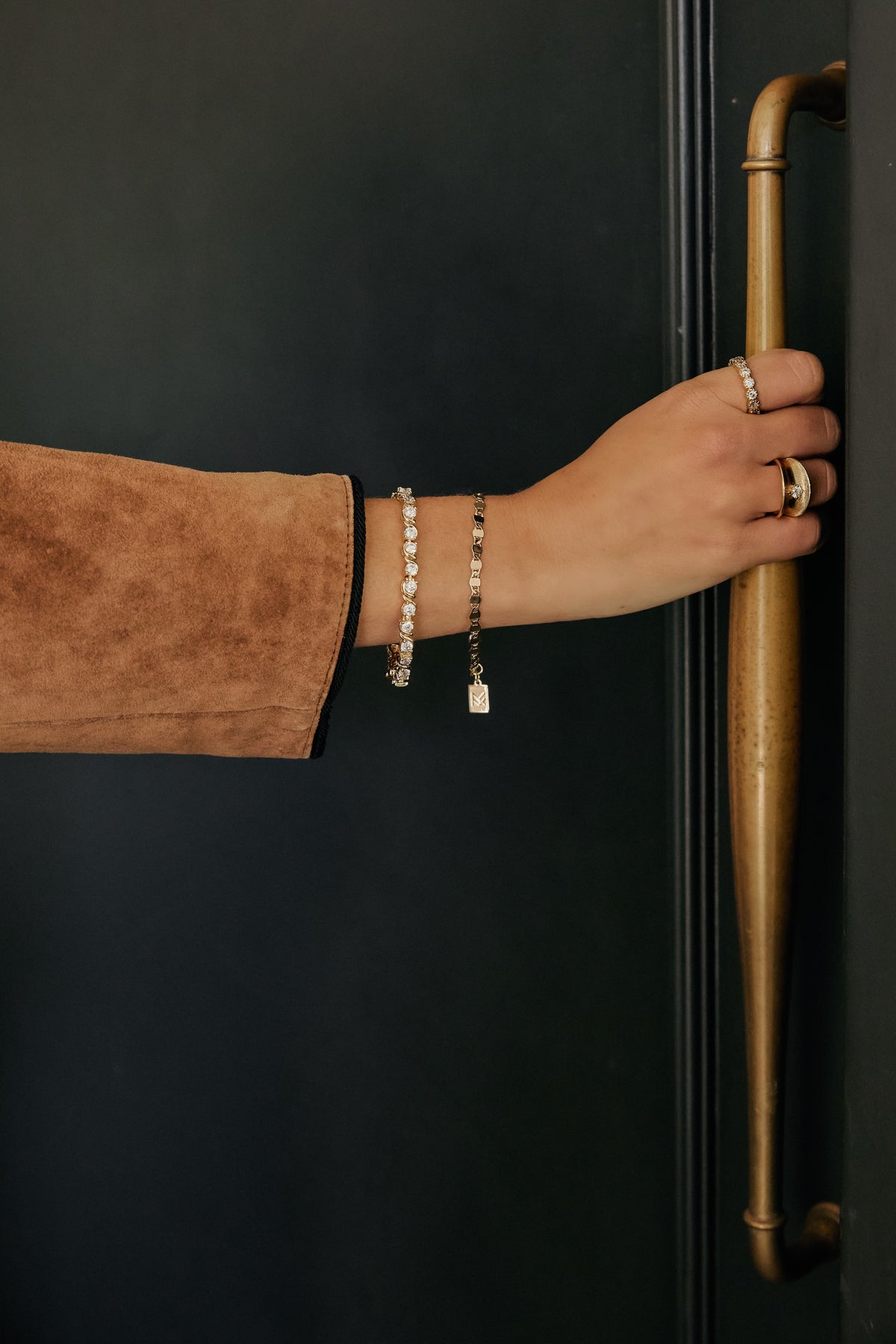 Model hand on door wearing gold Delilah bracelet, gold Ava bracelet, gold Isabelle ring and gold ann Marie ring