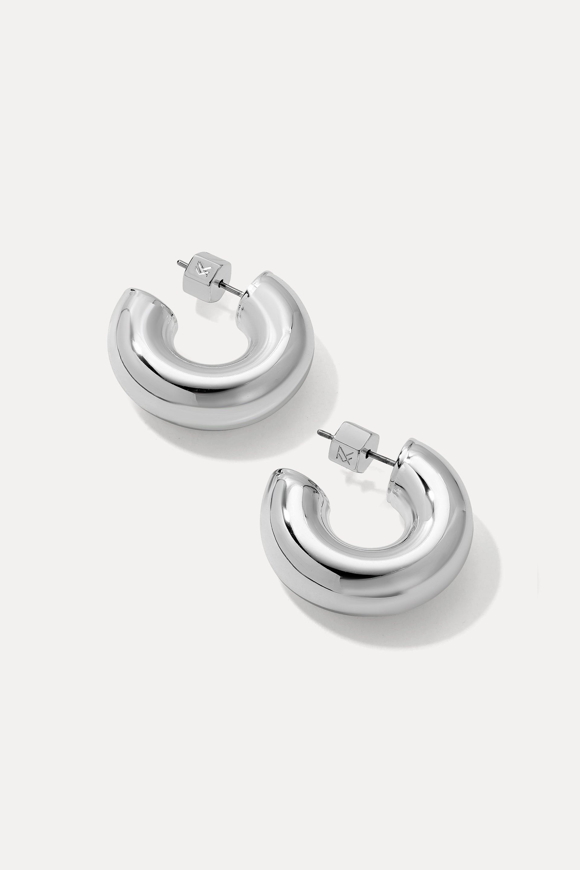Silver thick rounded Drew huggie hoop earrings displayed on a plain white background.