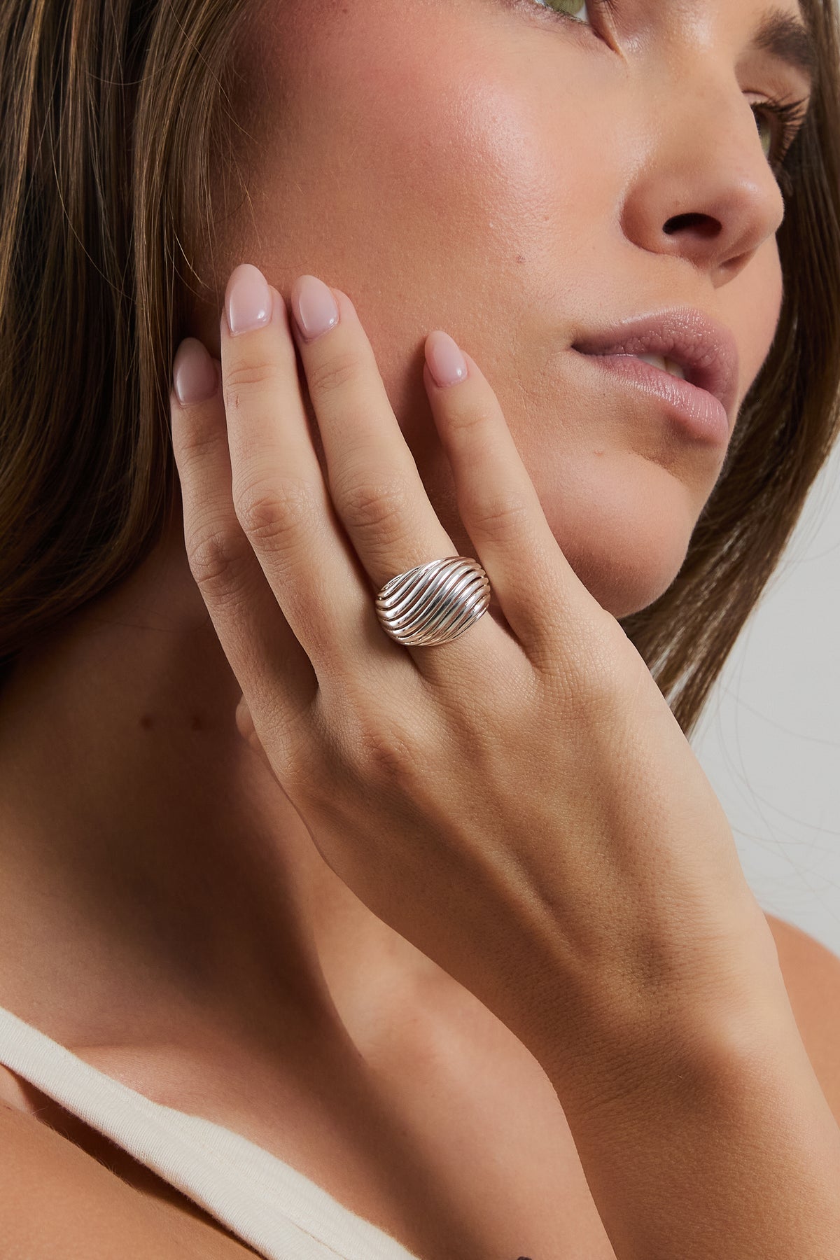 Model wearing silver Etta dome ring on index finger, resting hand against face in a cream ribbed top.
