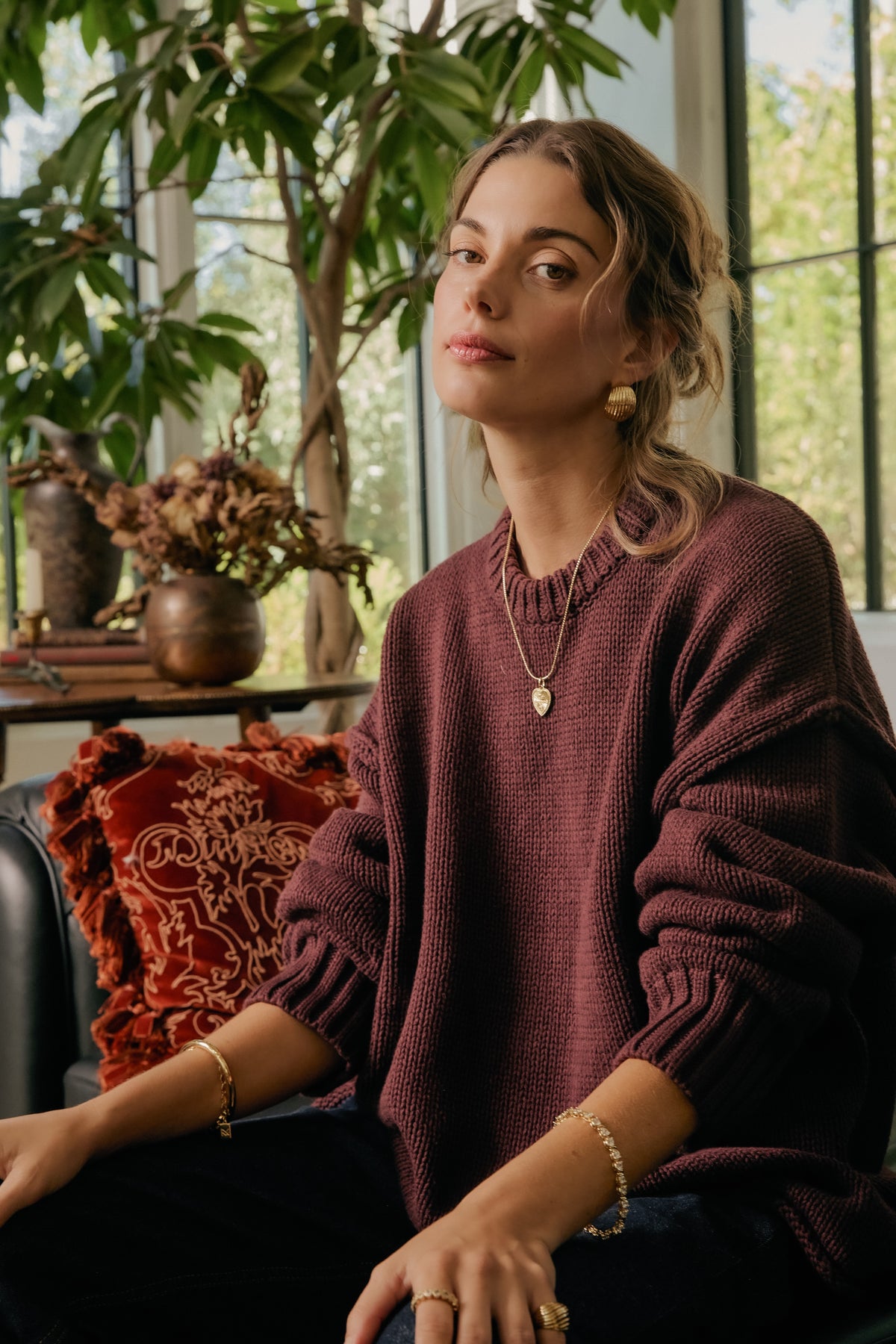 Model wearing gold Mina chain with Forever Charm heart pendant, Florence earrings, delilah bracelet, and Mina cuff in burgundy sweater.