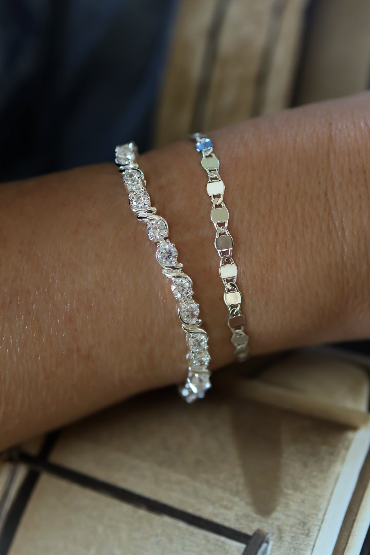 Close-up of model wearing stacked silver Delilah tennis bracelet and silver Ava mirror link chain bracelet.