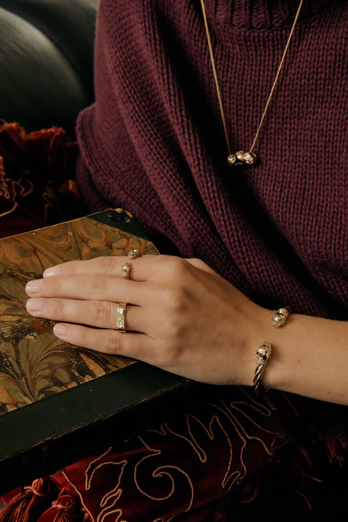 Model wearing gold Panther Cuff, Panther Ring, Mae Ring, and Josephine chain with Celeste Slider over a burgundy sweater
