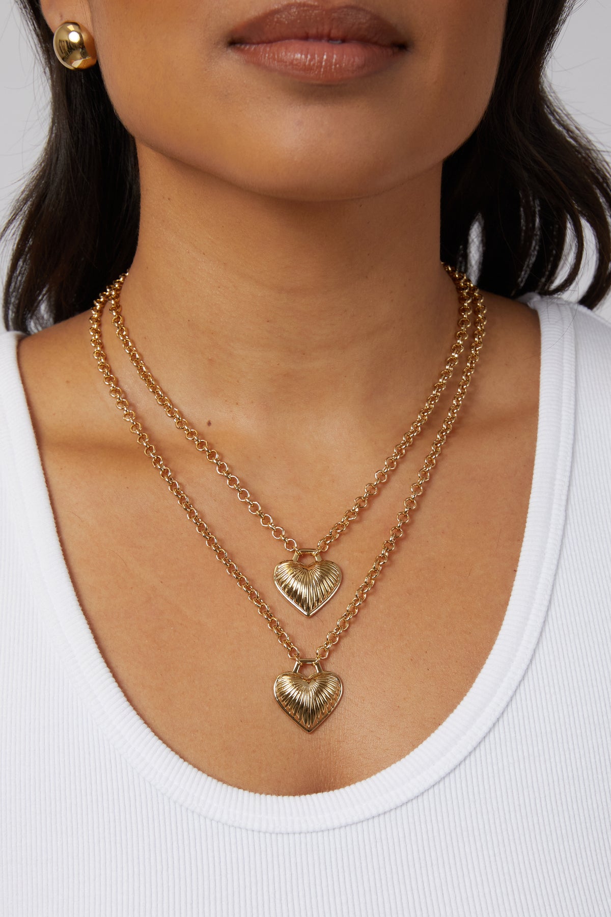 Model wearing two gold Juliet heart necklaces layered at different lengths.