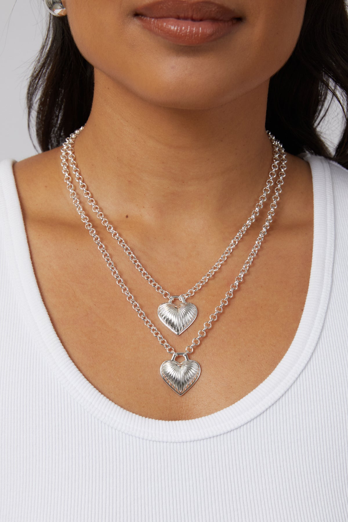 Model wearing two silver Juliet heart necklaces layered at different lengths.