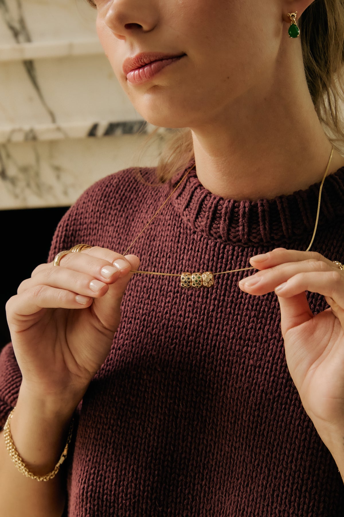 Model holding gold Josephine chain with clear, emerald and sapphire Celeste Slider charms, and gold panther emerald earring