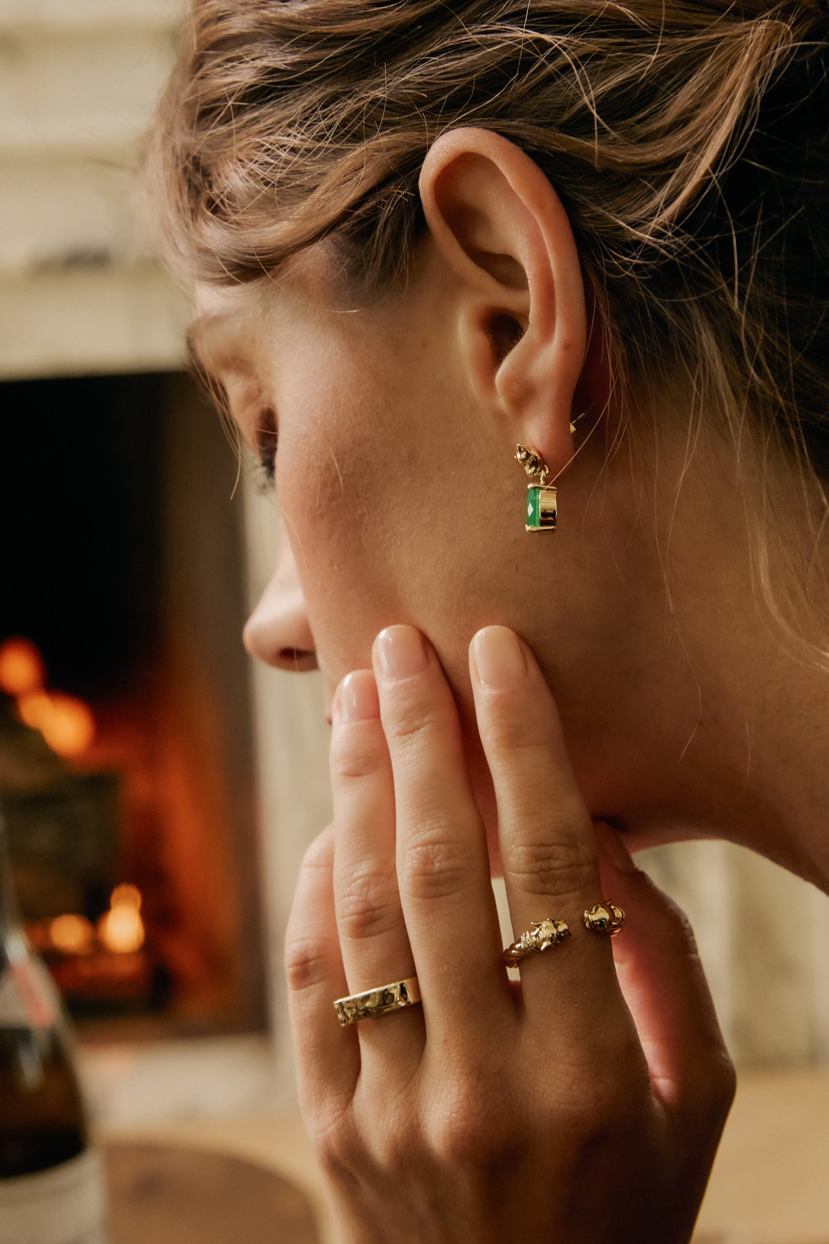 Model touching chin wearing Panther Emerald drop earring and gold Panther Ring with fireplace in background.