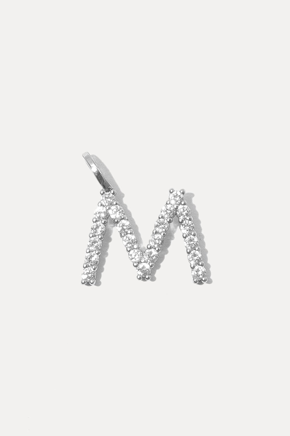 Silver pave initial charm in the letter M with crystal stones on a bail against a plain white background.
