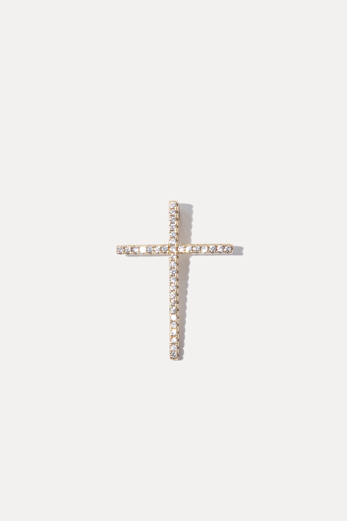 Gold cross charm set with sparkling clear cubic zirconia stones on a bail against a plain white background.