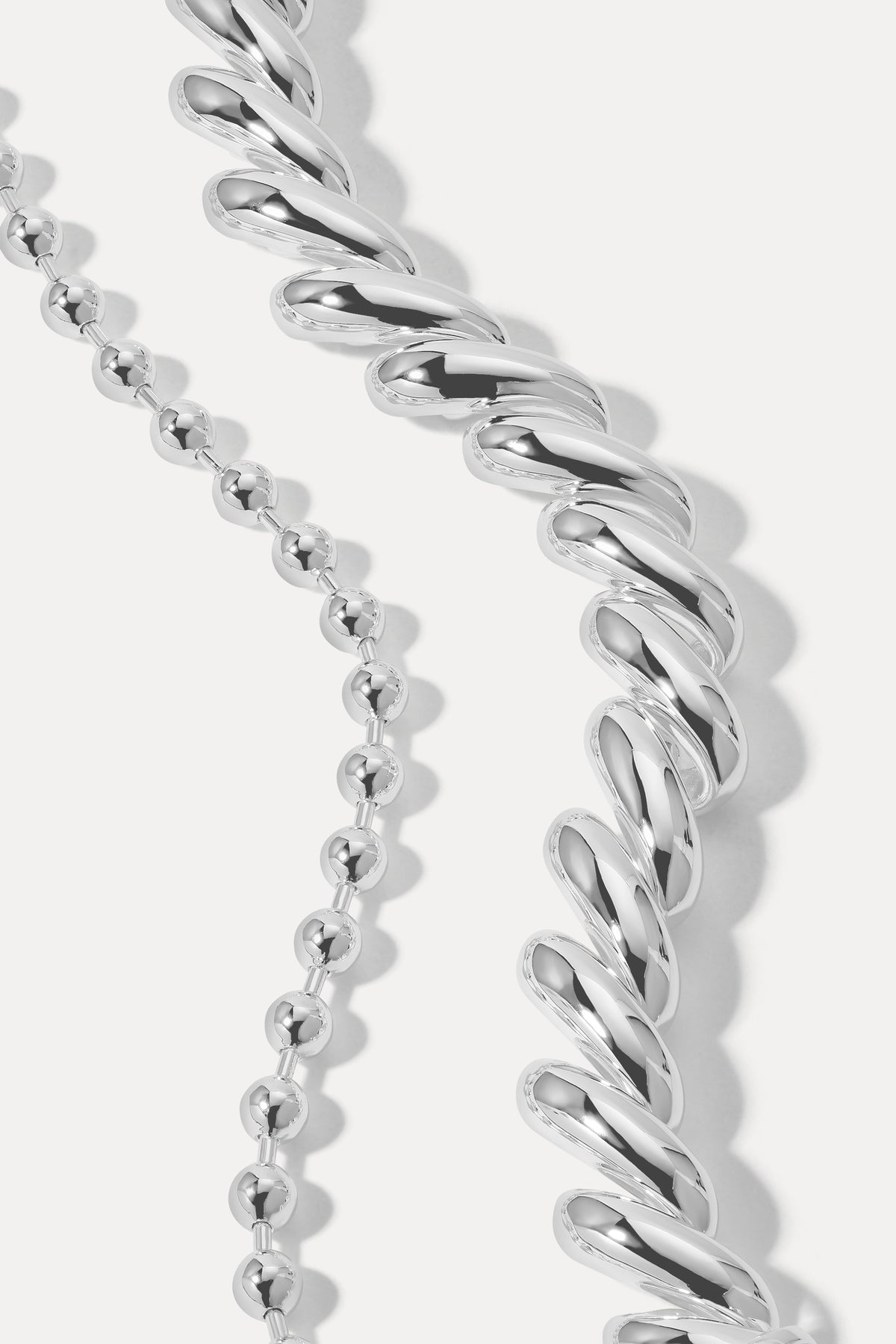 Silver layered bracelet stack combining ball chain and curb chain links on a plain white background.