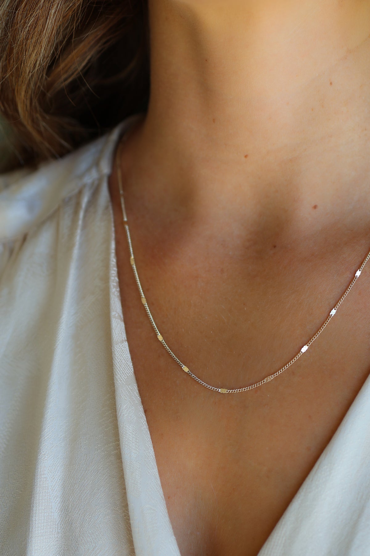Model wearing a white top showcasing the gold Coco cable chain necklace resting on her chest.