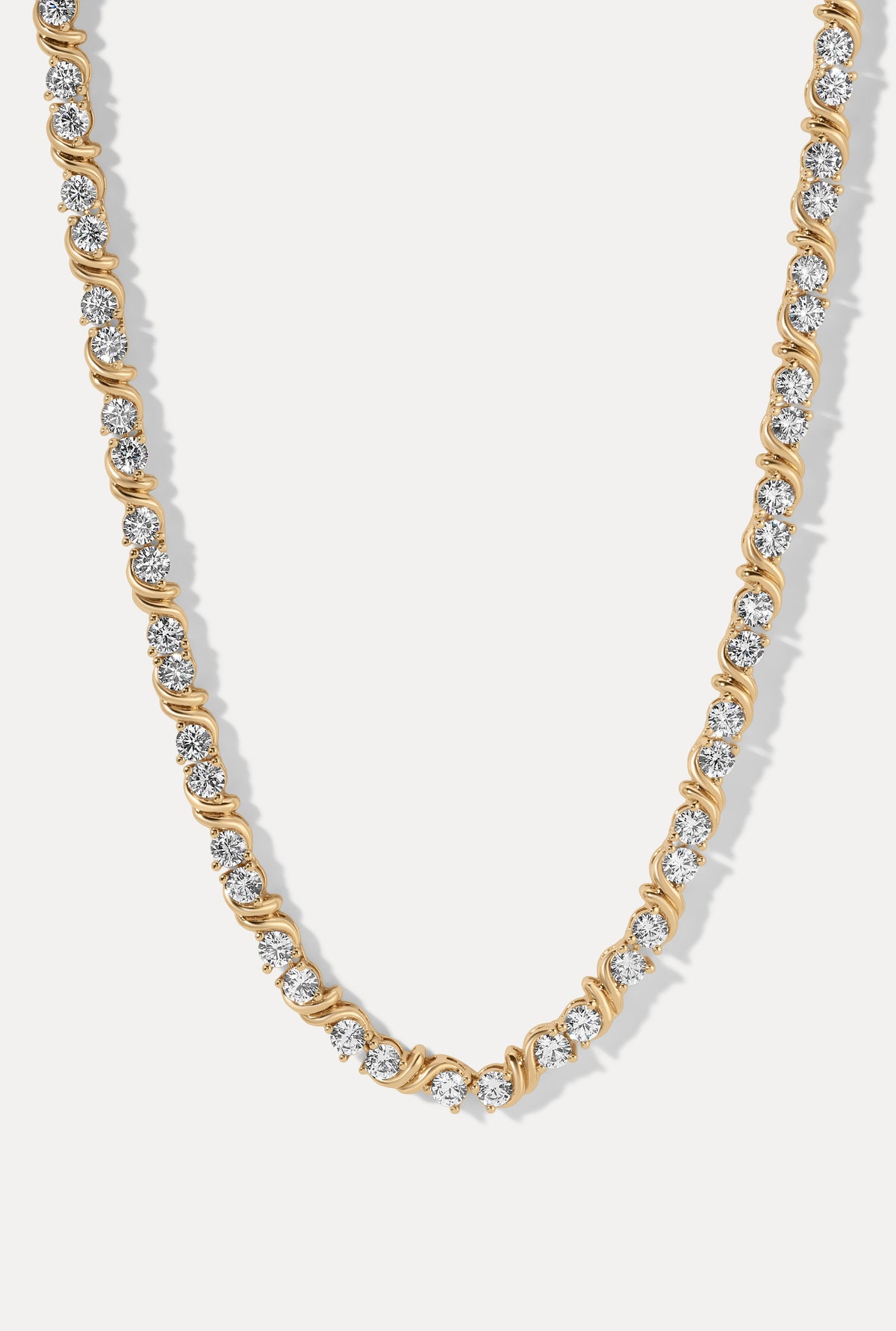 Gold Delilah tennis necklace featuring round CZ stones in S-link wave settings on a white background