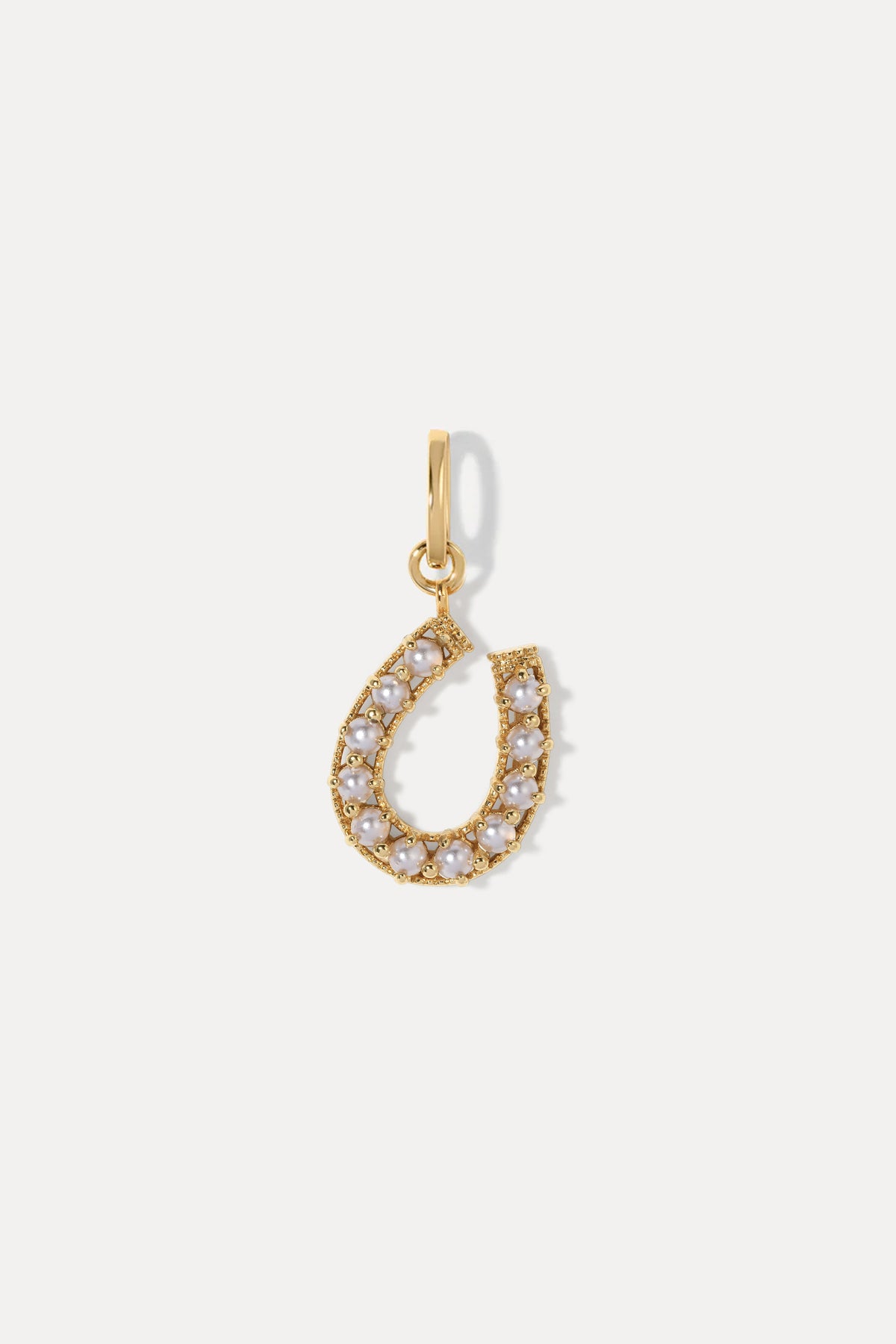 Gold horseshoe charm inset with small pearls on a bail against a plain white background.