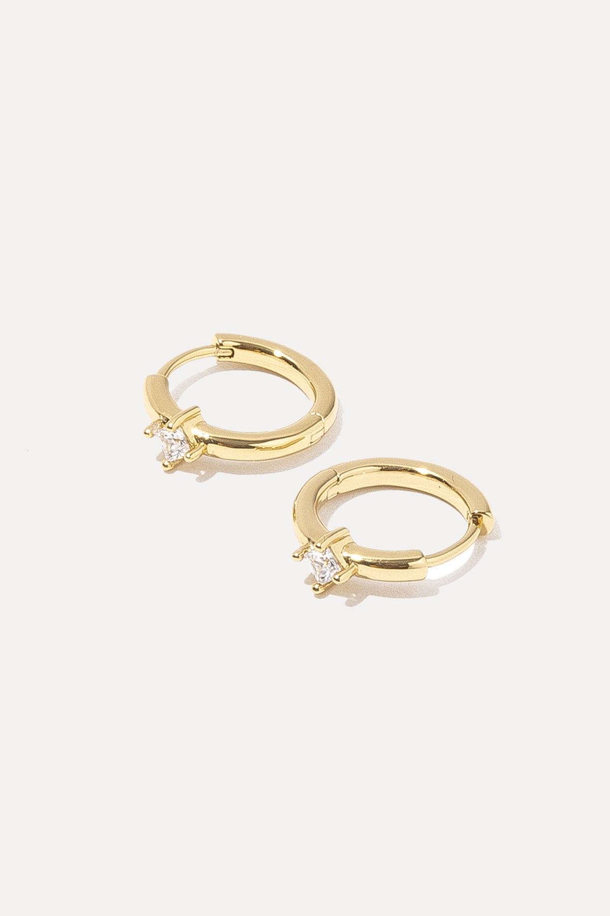 Pair of gold Kierza Huggies with cubic zirconia center stones on a white background.