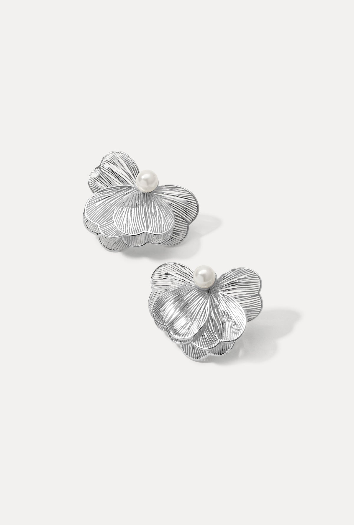 Pair of silver Lily Earrings featuring textured petal design with pearl centers on white.
