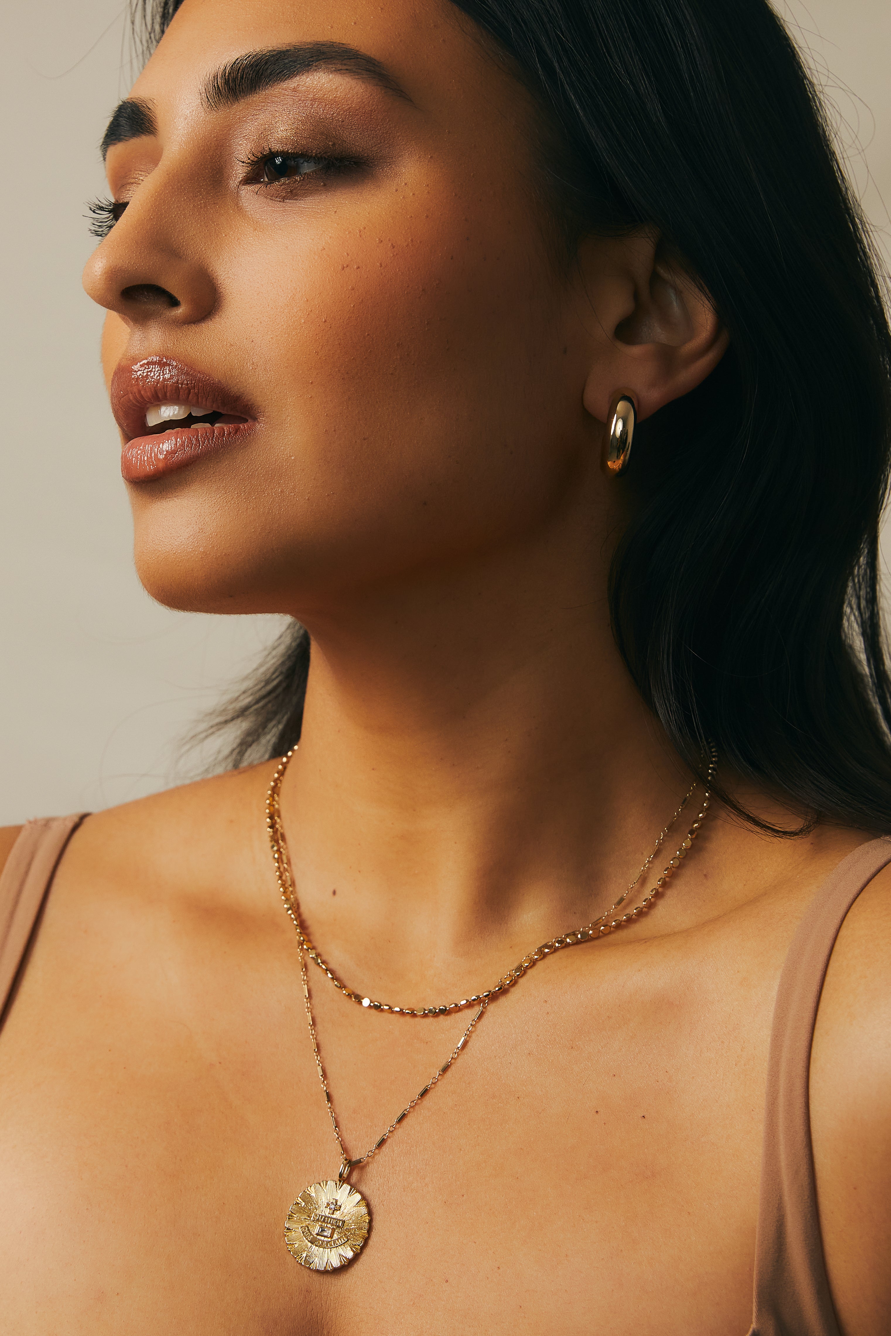 Close up of a model wearing the Lindsey chain and love charm in gold paired with the paisley necklace.