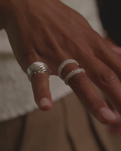Model wearing silver Etta dome ring on index finger, resting hand against face in a cream top.