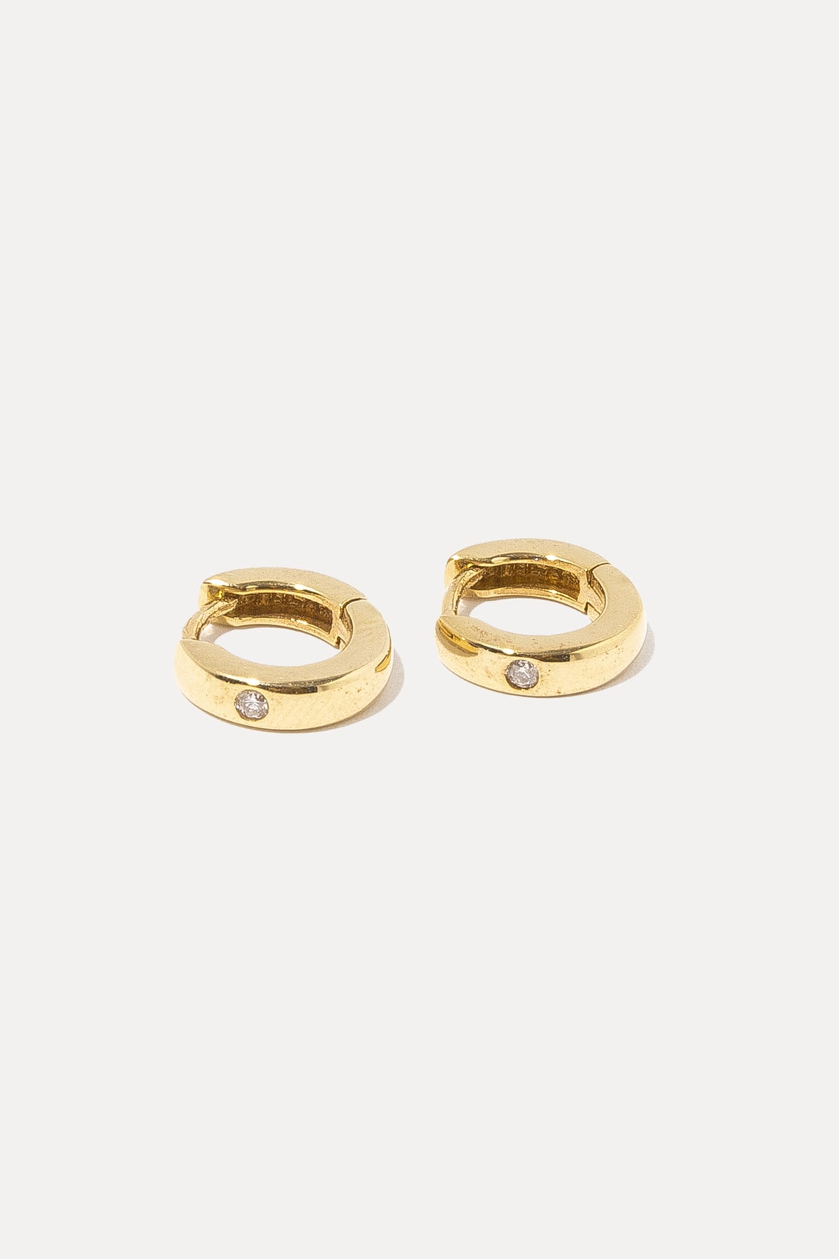 Pair of 14K gold solitaire diamond huggie hoop earrings displayed on a plain white background.