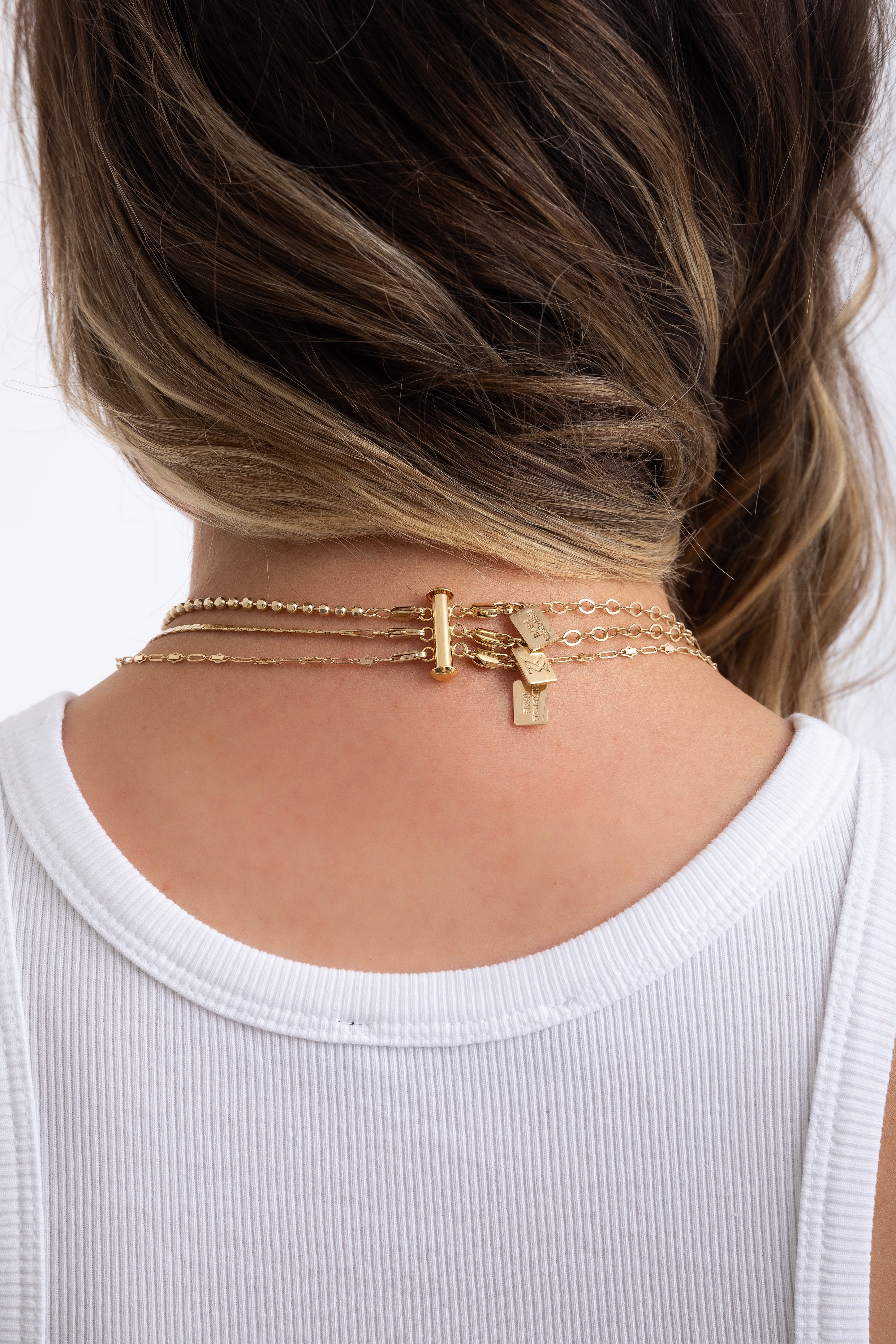 Back view of a model's neck showing the gold Layer Slayer clasp neatly holding multiple chains together.